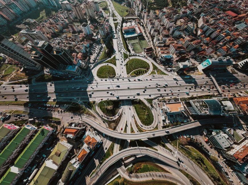 An overhead view of a diverse city with cars, buses, and green spaces, illustrating the complexities of urban navigation and the need for optimized routes.
