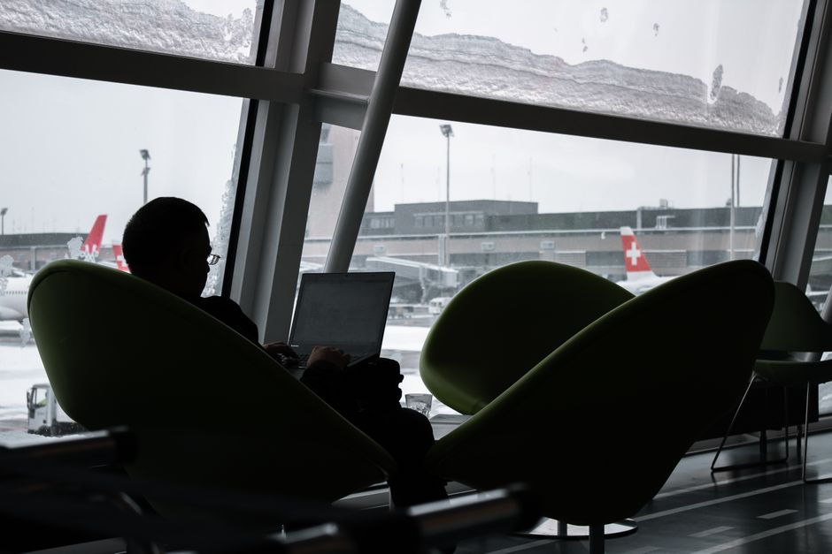 A person in an airport lounge working on a laptop and checking a phone, depicting efficient business travel.