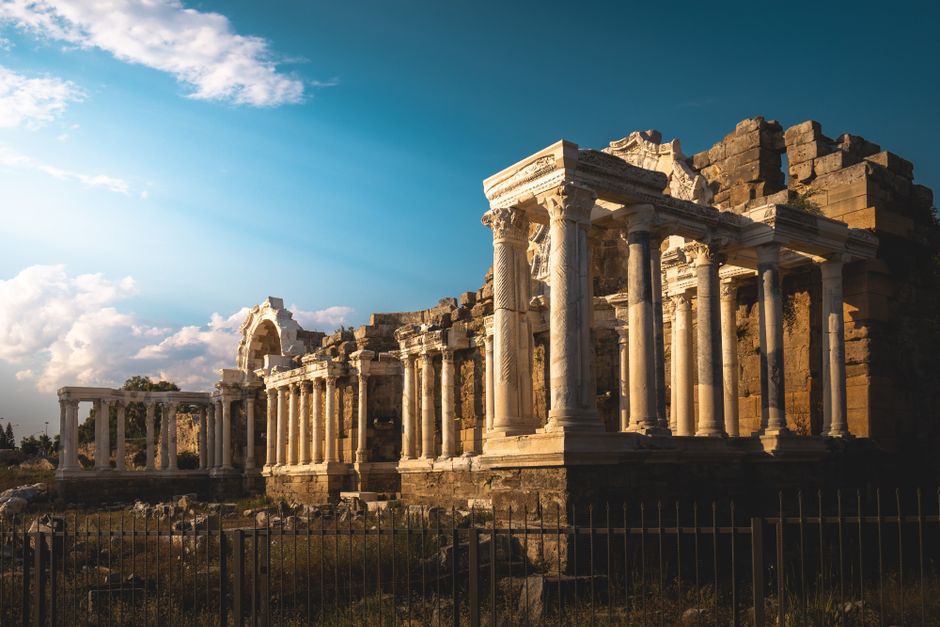 A digital rendering of ancient ruins, possibly a temple or coliseum, with a character exploring the site, evoking historical travel.