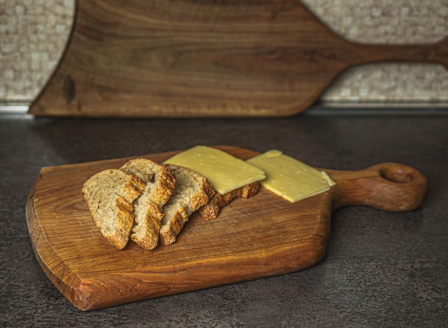 Close-up of a selection of artisan whole-grain breads and different types of cheese, such as feta and aged cheddar, on a rustic wooden board.