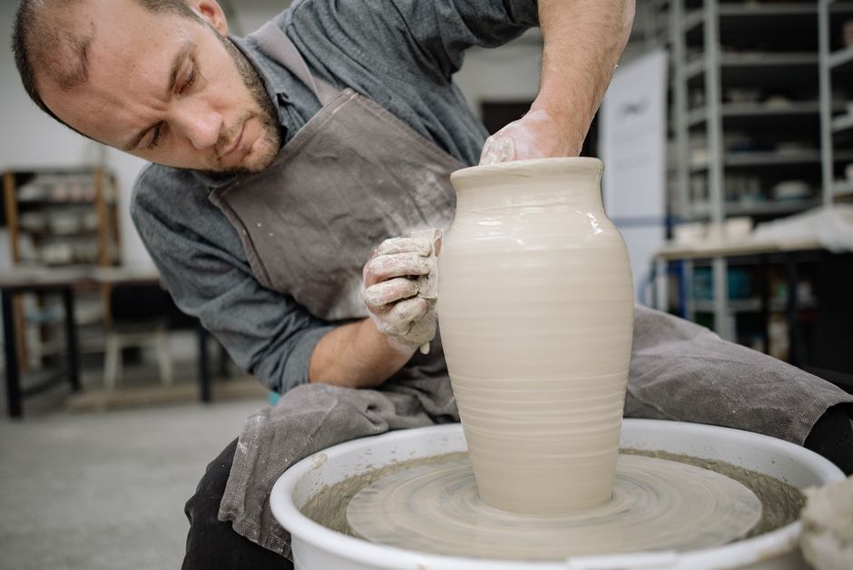 Close-up of a potter's hands shaping clay on a wheel in a bright, sunlit studio, surrounded by finished ceramic pieces.