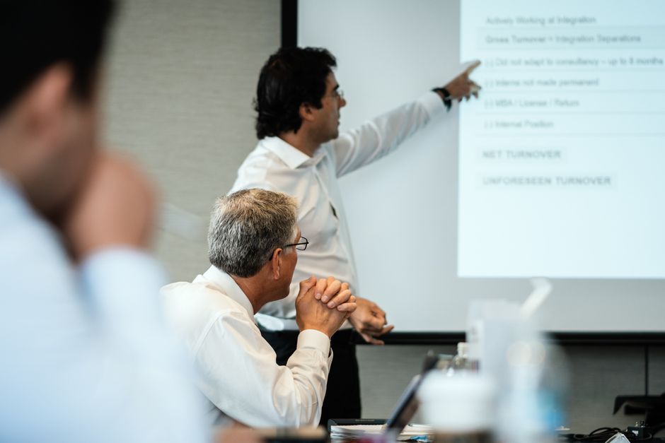 A diverse business team in a modern office looking at charts on a screen, with one person pointing and explaining AI-driven insights to clients.