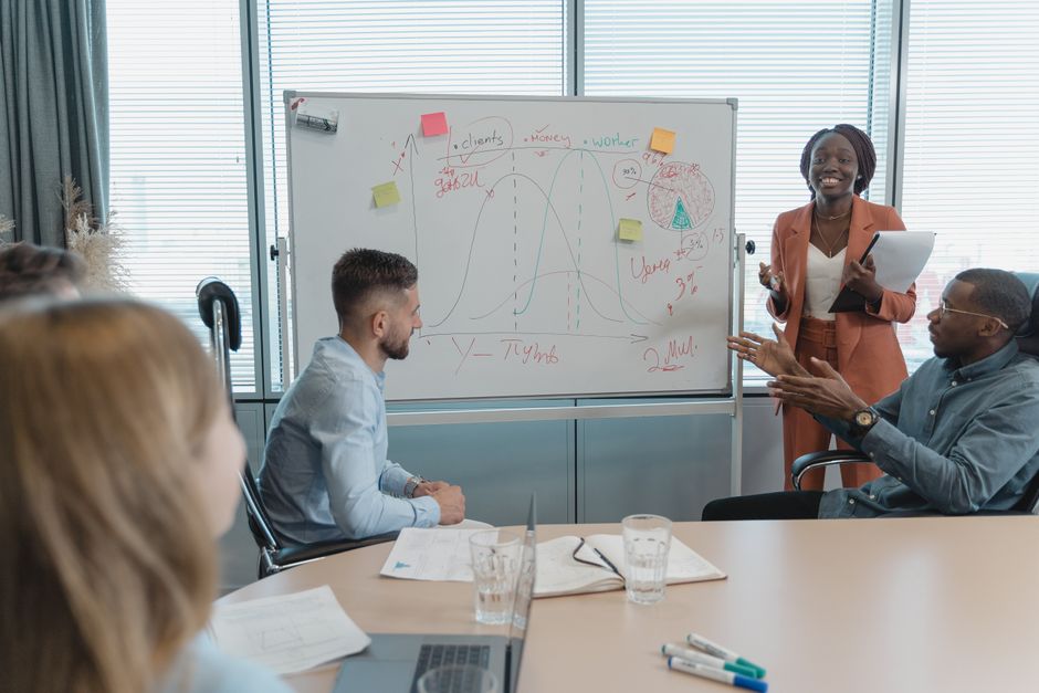 A team of diverse individuals looking at a whiteboard covered with a business strategy, market segments, and resource allocation charts.