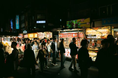 A vibrant, bustling street food market in Southeast Asia, with various food stalls and people mingling, capturing the energy of spontaneous dining.