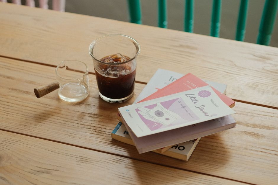 Someone enjoying coffee and a book at a cozy cafe, wearing a comfortable yet stylish layered outfit with an elegant bag nearby.