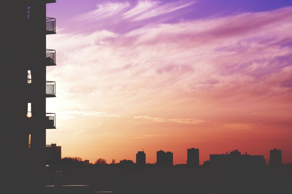A serene city skyline at dusk, with soft lights appearing, viewed from a high-rise balcony, suggesting calm after a busy day.