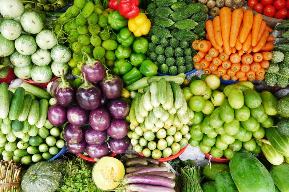 A close-up of a vibrant display of seasonal fruits and vegetables, like tomatoes, peppers, and greens, at a farmers market.