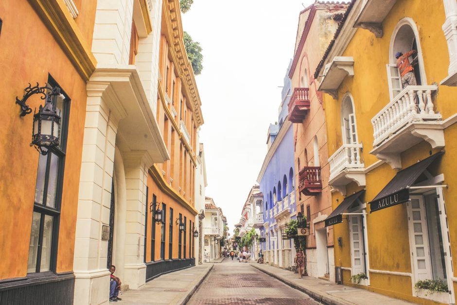 A vibrant, colorful colonial street in Cartagena, Colombia, with intricate balconies and a person sitting on a stoop reading a book, capturing the essence of a literary city break in South America.