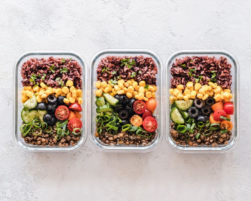 Various clear food containers filled with simple, prepped ingredients like chopped vegetables, boiled eggs, and fruit, ready for the week.