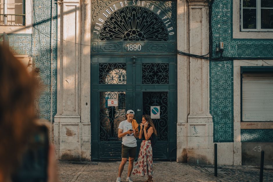 A smiling couple browsing vibrant stalls at a bustling open-air market in Lisbon, interacting with a local vendor.