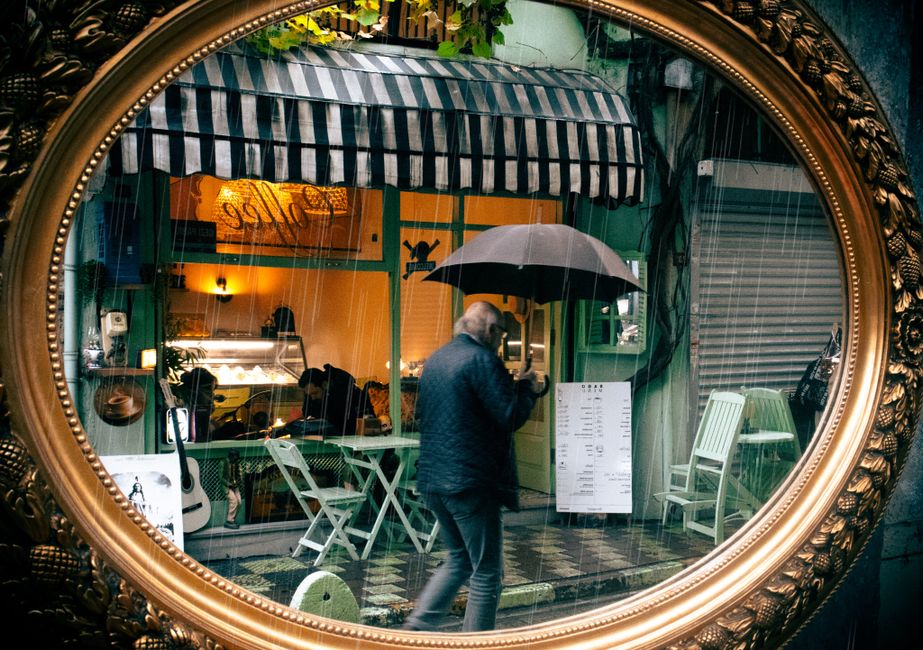 A person reading a book by a window in a cozy cafe, rain streaking down the glass outside.