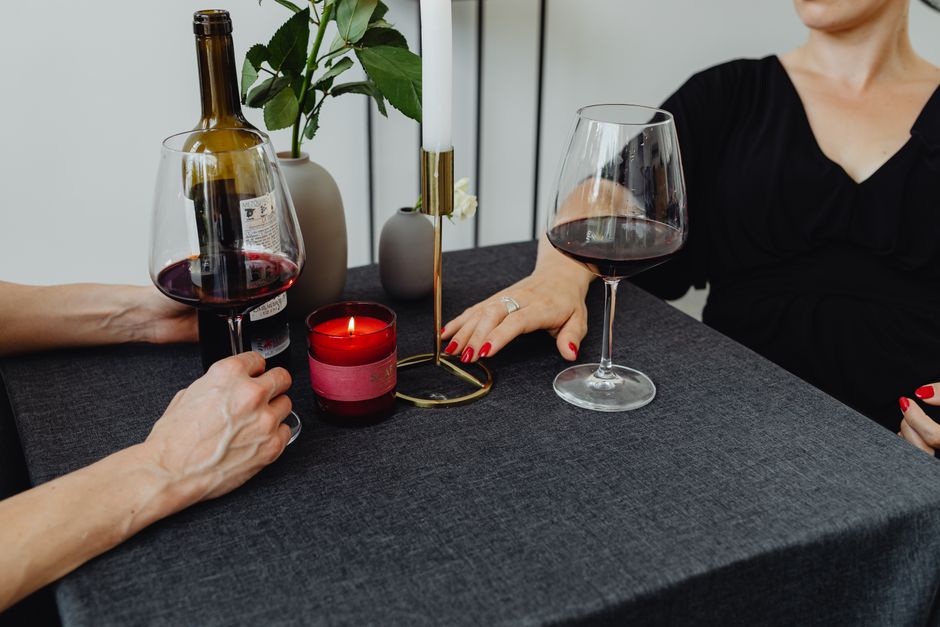 A cozy dinner table set simply with a few candles, a bottle of red wine, and a one-pot dish, reflecting relaxed home entertaining.