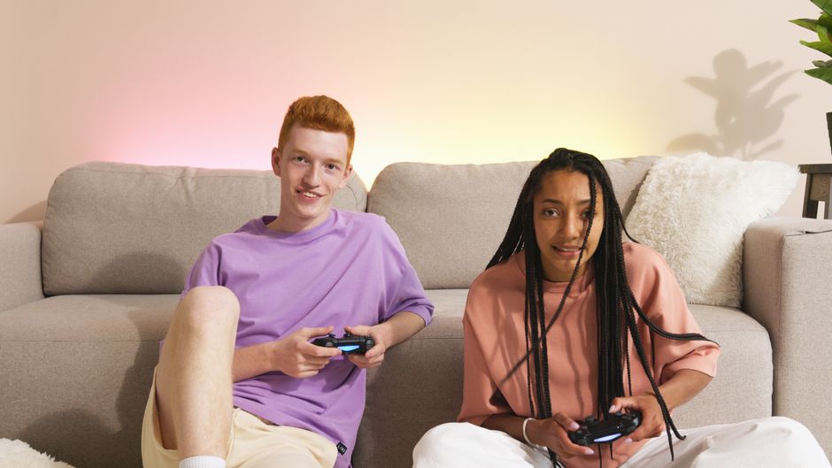 A wide shot of a comfortable, small living room with two people intently playing a co-op game on a large TV, controllers in hand.