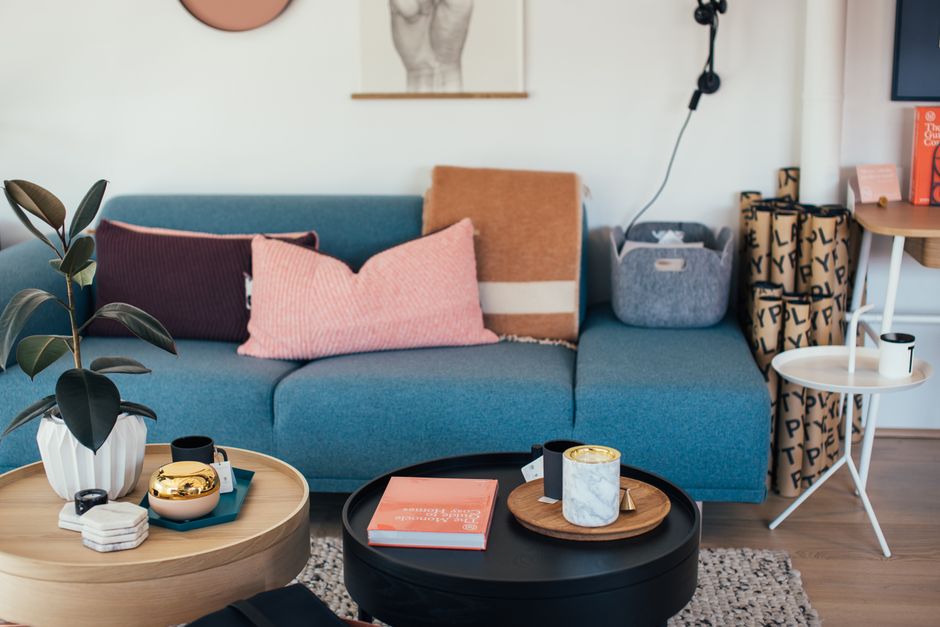 A cozy living room featuring a mix of vintage and modern furniture, with personal photographs, books, and unique decorative objects displayed on shelves and coffee tables.