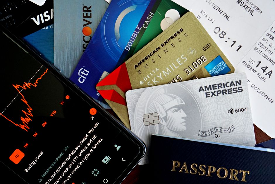 A person reviewing physical bank statements and an open mobile app, indicating a process of identifying recurring tech subscription charges.