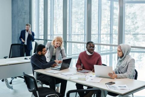 Diverse team of small business professionals collaborating around a table with laptops, illustrating effective meeting dynamics.