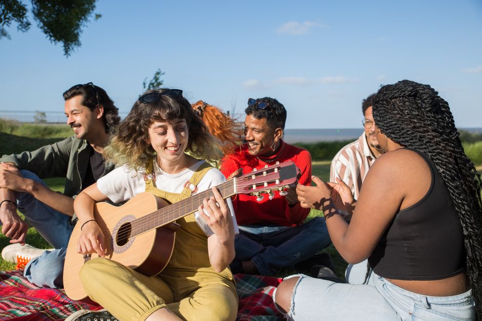 A diverse group of friends laughing and sharing food at a picnic in a sunny park, illustrating joyful, low-cost social activities.