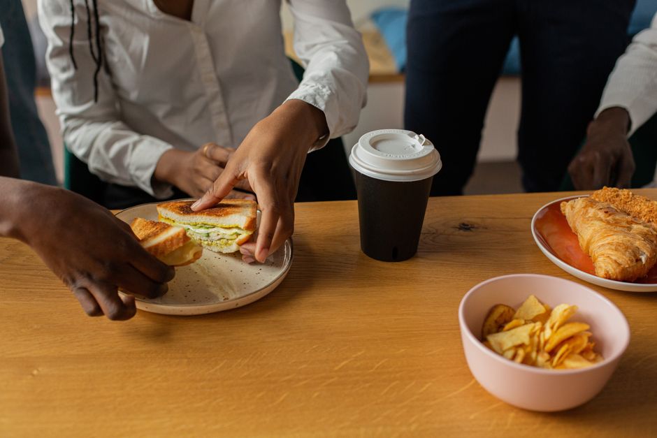 Three colleagues in a modern office kitchen sharing a healthy, colorful lunch, actively conversing and not looking at screens, depicting a mindful break.