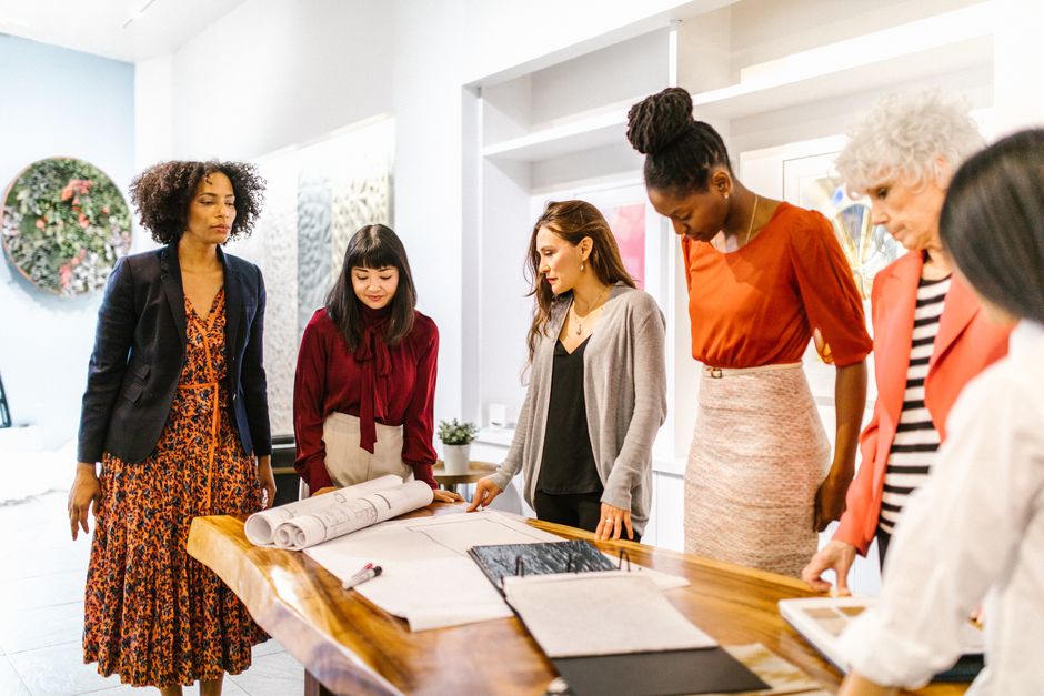 Three creative professionals from diverse backgrounds discussing design concepts around a table in a modern office, symbolizing the target audience.