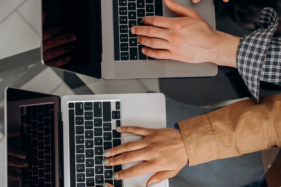 Multiple hands from different people, each resting on a laptop keyboard, with faint global map overlays, illustrating the interconnectedness of global teams and the role of translation tools.
