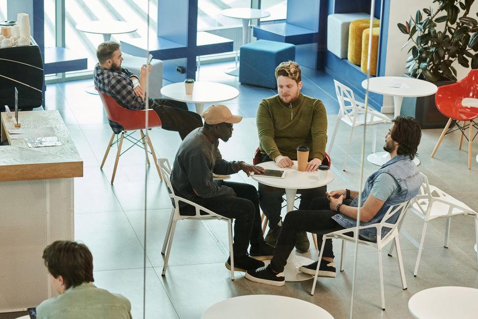 A group of young adults from diverse backgrounds laughing and chatting over coffee in a bright, modern cafe, showing new friendships forming in a community setting.