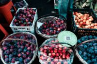 A vibrant display of colorful, fresh seasonal fruits and vegetables at a bustling farmers market stand, showcasing local abundance.