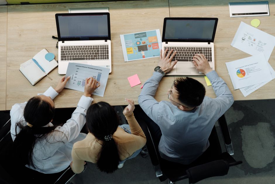 A diverse team of professionals working together around a table with laptops, illustrating collaborative use of AI prompt libraries to streamline office tasks.
