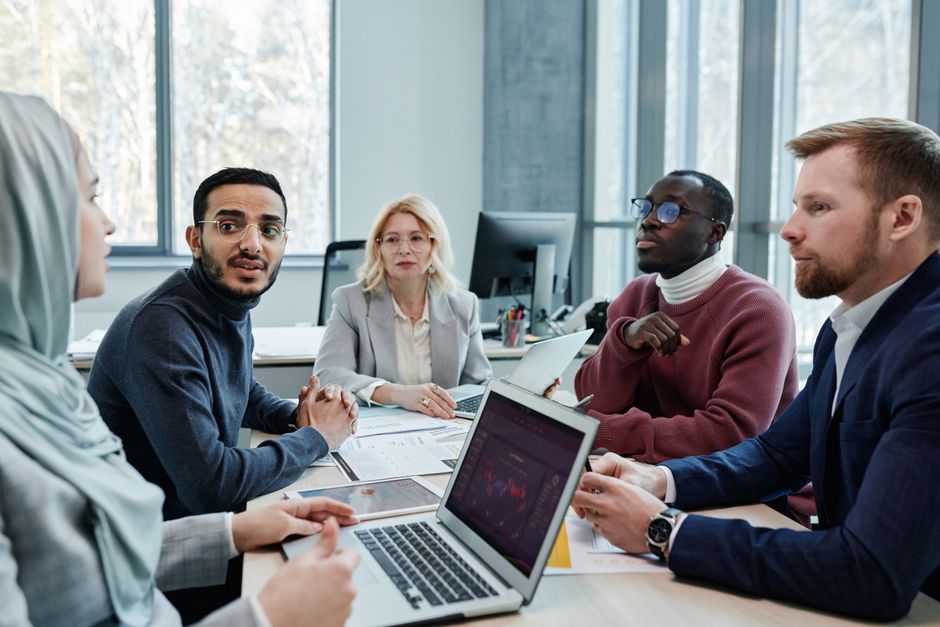 A diverse group of business professionals in a modern office, engaged in a discussion about project budgets and proposals, representing negotiation.