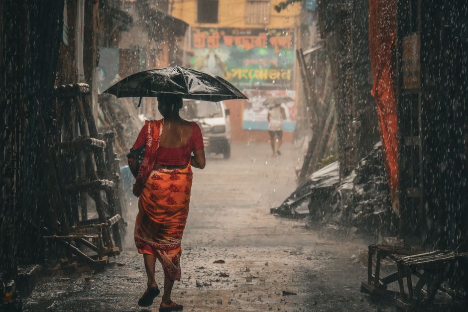 A woman in a chic, lightweight summer outfit with a striped linen shirt and dark, flowing trousers, paired with comfortable sandals, walking confidently through a sunny, humid city street, showcasing practical elegance.