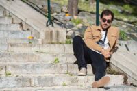 An exhausted tourist sitting on stone steps in a bustling European city, looking overwhelmed amidst crowds and historic architecture.