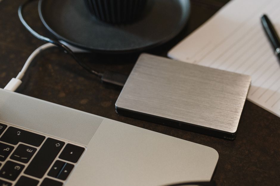 A rugged, portable external SSD connected via USB-C to a modern laptop, symbolizing local backup and data transfer for travelers and families.
