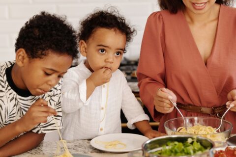 A family, including a child and parents, happily cooking a healthy dinner together in a modern kitchen, chopping vegetables and smiling.