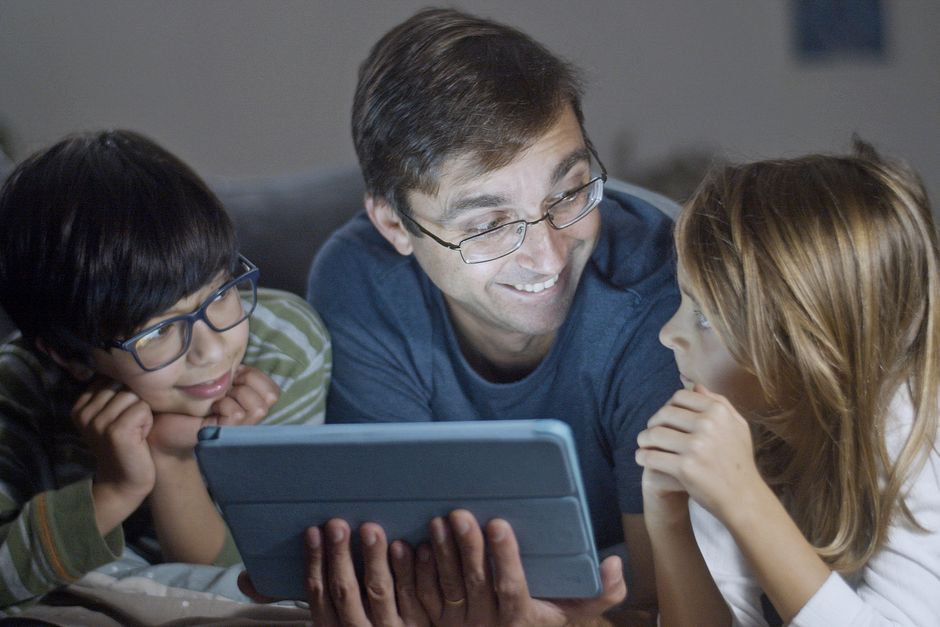 A diverse family, including parents and children, gathered around a kitchen table, smiling as they collaboratively view a shared digital calendar on a tablet.