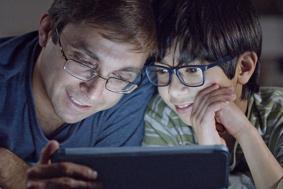 A multi-generational family, perhaps in Europe, gathered around a tablet, joyfully viewing and curating old family photos, depicting connection and shared memories.