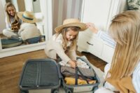 A family, including a mother and two children, packing electronics like tablets and phones into a suitcase, preparing for an international trip.