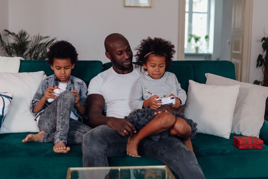 A diverse family (parents and two children) laughing and playing a cooperative video game on a console, showcasing the social aspect of gaming and varied mood experiences.