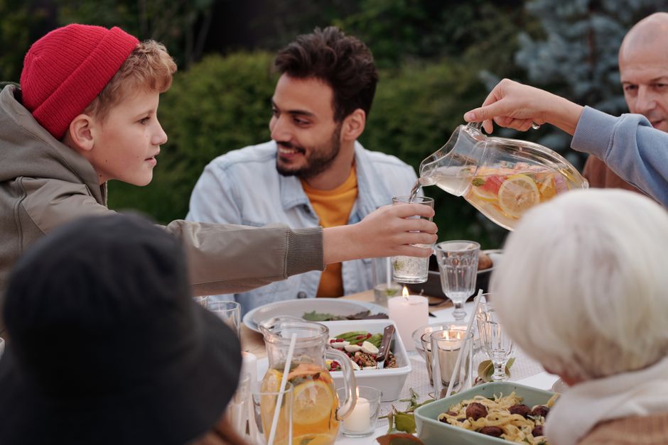 A diverse family laughing and conversing around a dinner table, with serving dishes in the center and no visible phones.