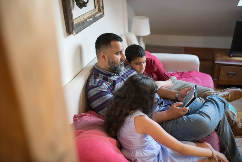 A family member sharing a tablet with a child, showing icons for apps and settings on the screen.