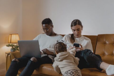 A family, including a mother, father, and two children, happily using various refurbished phones and laptops in their living room, demonstrating affordable tech access.