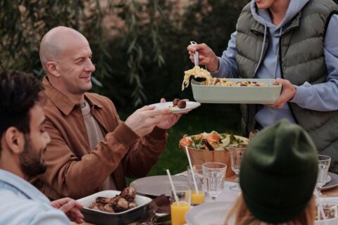 Friends laughing and sharing a simple meal around a rustic dining table, lit by warm candlelight, symbolizing easy entertaining.