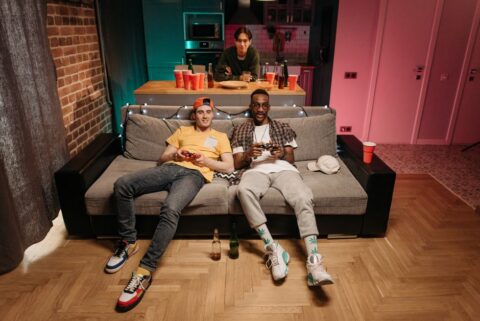 A diverse group of friends laughing while playing a cooperative video game on a large TV in a modern living room, with snacks and drinks nearby.