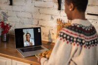 Two young women on separate laptop screens smiling and talking, illustrating long-distance friendship.