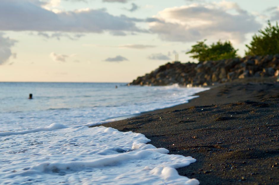 A serene sunset over a white sand beach in Guadeloupe with palm trees silhouetted against the sky.