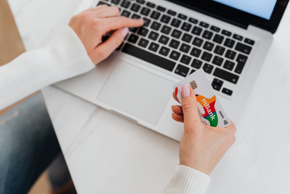A close-up shot of a hand holding a credit card, typing details into a laptop for an online purchase, with a world map faintly visible in the background.