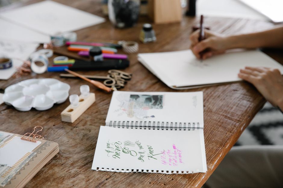 A close-up shot of a hand holding a fountain pen, poised over the textured page of an open travel journal, with blurred historic European architecture in the background, conveying the act of capturing travel memories.