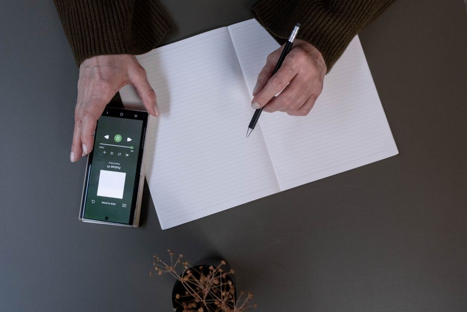 A close-up shot of a hand holding a smartphone over a physical notebook, using a scanning app to digitize handwritten notes on a page, showing the process of bridging analog to digital.