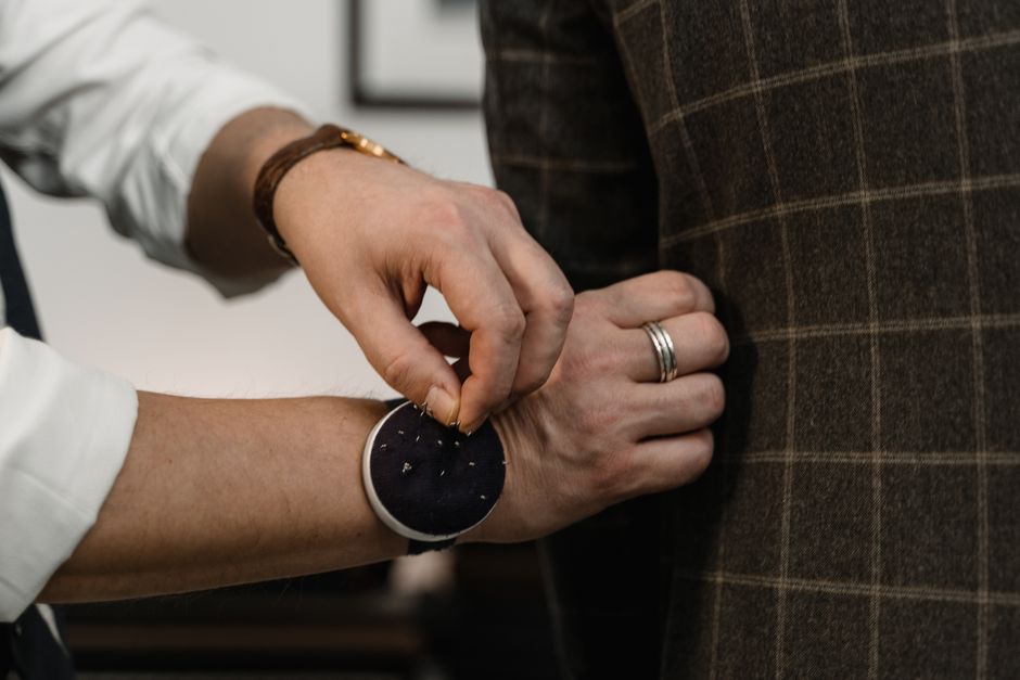 Close-up of a tailor's hands adjusting and pinning the sleeve length of a blazer on a customer, highlighting precision tailoring.