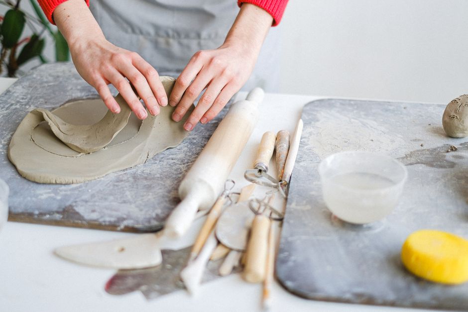 Close-up of a pair of hands on a potter's wheel, carefully shaping clay, with a blurred background of a workshop.