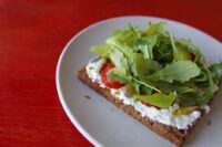 A beautifully arranged healthy lunch featuring a slice of whole-grain sourdough with goat cheese, alongside a vibrant salad with mixed greens, cherry tomatoes, and cucumber.