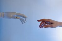 A human hand and a robotic hand gently touching, symbolizing ethical AI collaboration and partnership in client work.